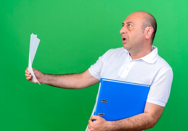 looking-side-scared-casual-mature-man-holding-folder-with-paper-isolated-green-background_141793-63577